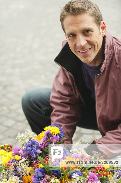 Mann kauernd von Blumen  lächelnd  Portrait