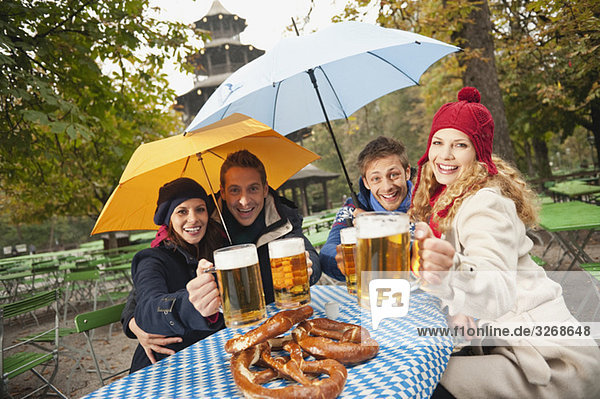 Deutschland  Bayern  Englischer Garten  Vier Personen sitzend im verregneten Biergarten