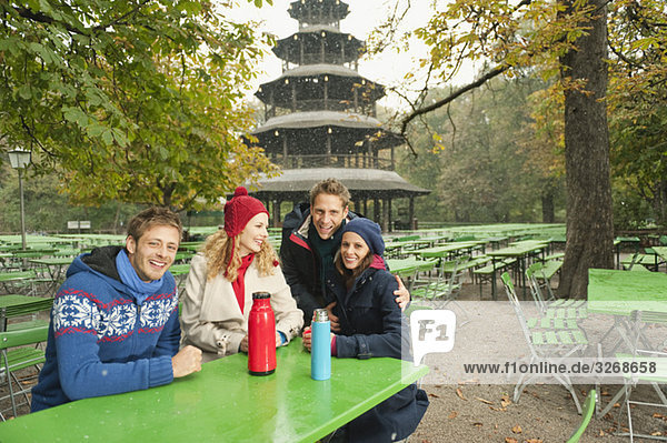 Deutschland  Bayern  Englischer Garten  Biergarten  Vier sitzen im Biergarten  Chinesischer Turm im Hintergrund