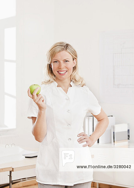 Frau im weißen Laborkittel mit Apfel