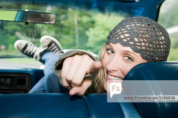 Young woman in car pointing at camera