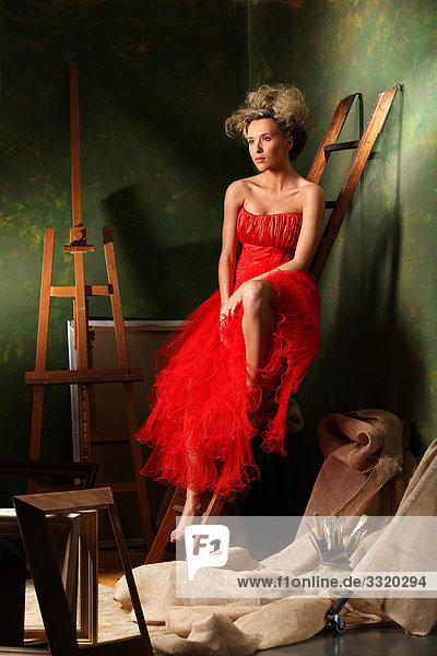Frau im roten Kleid auf einer Leiter sitzend