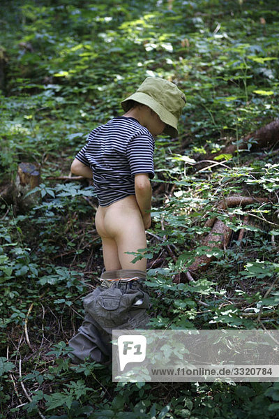 Ein kleiner Junge  der in den Wald pinkelt.
