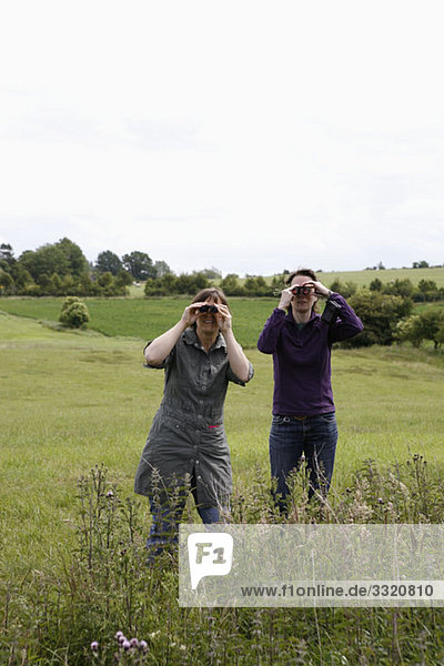 Two women standing in a field and using binoculars