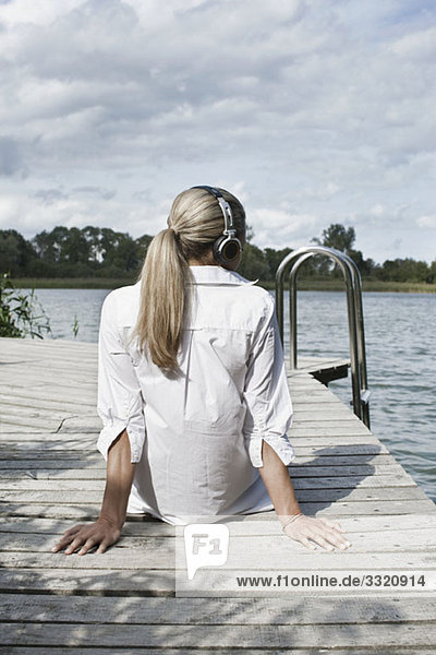 A woman wearing headphones relaxing on a jetty