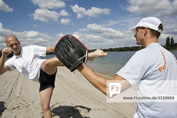Ein Mann beim Kickboxen mit einem Personal Trainer am Strand.