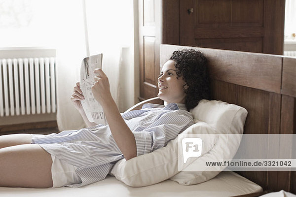 A woman lying on her bed and reading the newspaper