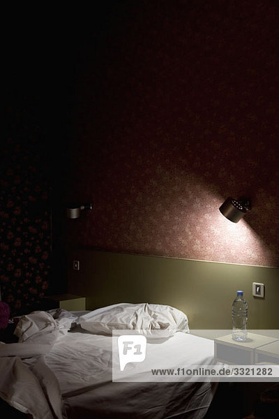 Ein ungemachtes Bett  das nachts von einer Lampe beleuchtet wird.