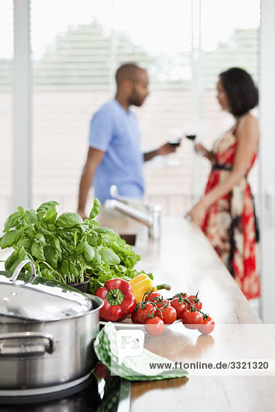 Frische Produkte auf einer Küchentheke und ein junges Paar im Hintergrund