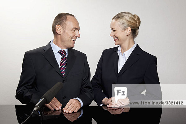 Ein Mann und eine Frau sitzen am Schreibtisch mit einem Mikrofon.