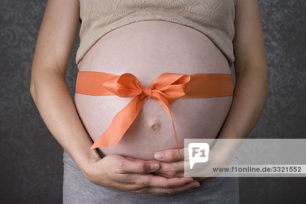 Ein Band in einer Schleife um einen schwangeren Bauch gebunden  Mittelteil  Fokus auf den Bauch