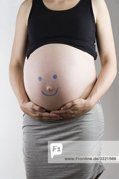 Ein Smiley auf einen schwangeren Bauch gezeichnet  Mittelteil  Fokus auf den Bauch