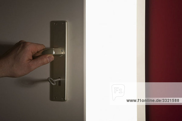 Detail einer Hand  die eine Tür zu einem hellen Raum öffnet.