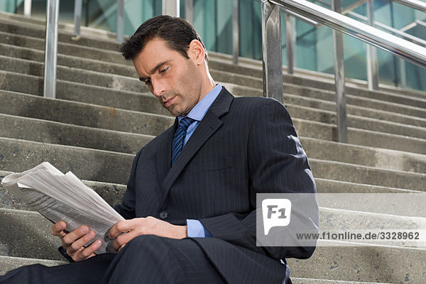 A businessman sitting on steps with a newspaper