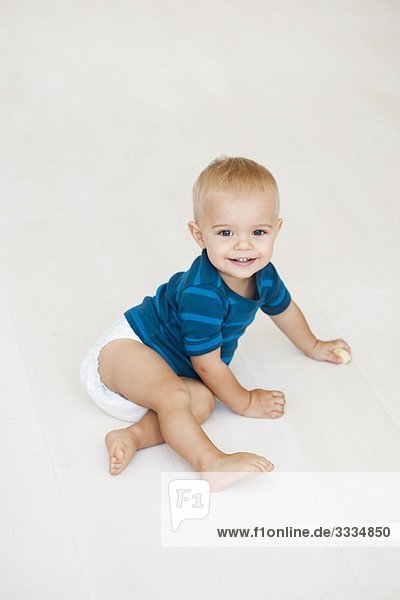 Baby sitzend auf dem Boden in Windeln