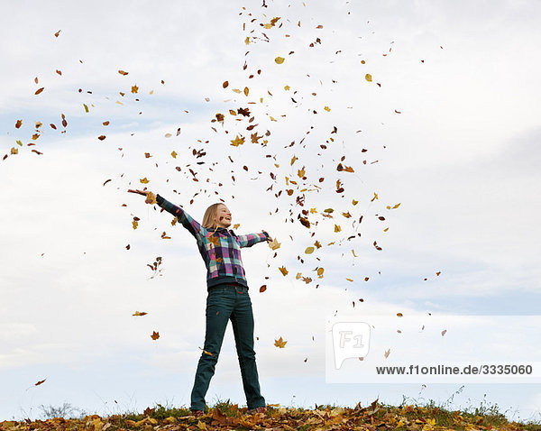 Mädchen wirft Herbstlaub in die Luft