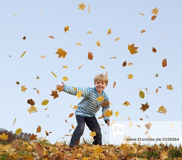 Junge wirft Herbstlaub in die Luft