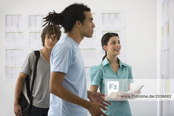 Male college student staring with disbelief at results posted on bulletin board  friends watching in background
