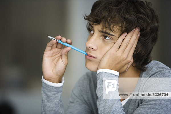 Young man daydreaming  absently holding pen in mouth