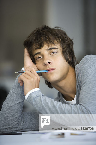 Young man leaning on elbow  pen in mouth  looking at camera with bored expression