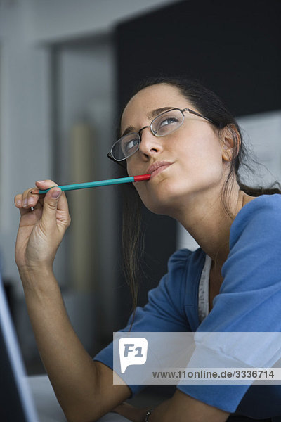 Woman contemplatively looking away with pen in mouth