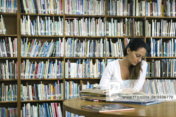 Woman reading book at table in library