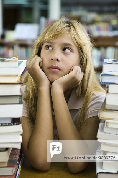 Preteen Mädchen sitzend mit zwei großen Stapeln von Büchern  Kinn in den Händen  wegschauend