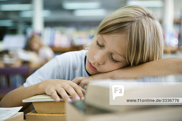 Jungenschlaf mit Kopf auf den Armen in der Bibliothek