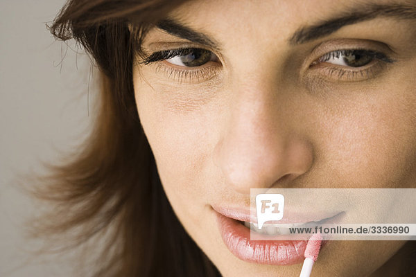 Junge Frau beim Auftragen von Lippenglanz mit Lippenpinsel und Mund