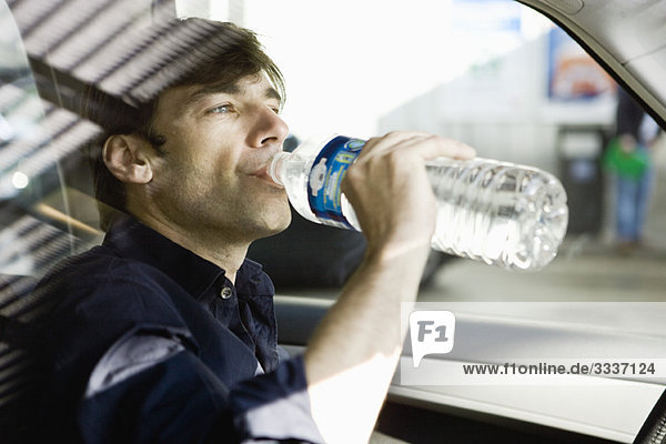 Mann trinkt während der Fahrt Wasser in Flaschen