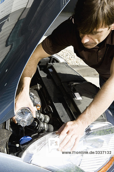 Mann gießt Wasser in den Kühler eines überhitzten Autos