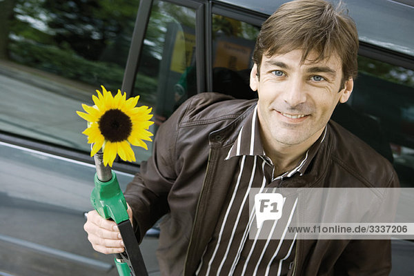 Mann an der Tankstelle hält Gasdüse mit austretender Sonnenblume