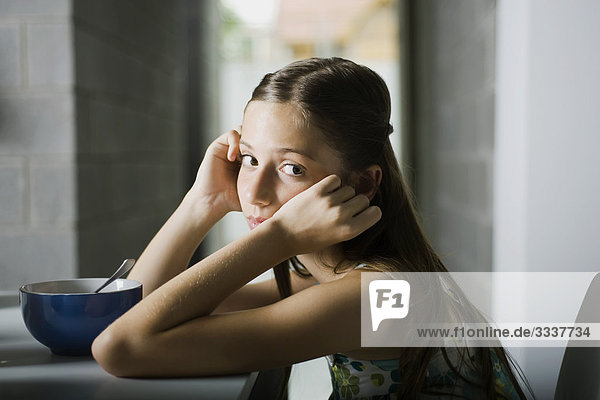 Girl sitting at table with head in hands  looking sulkily at camera