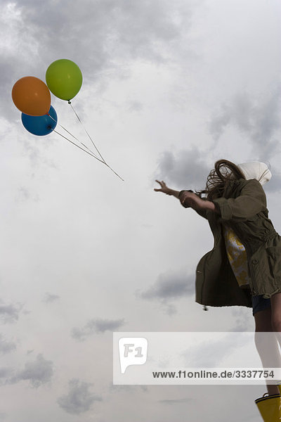 Eine Frau beobachtet  wie ein Haufen Luftballons in den bewölkten Himmel schwebt.