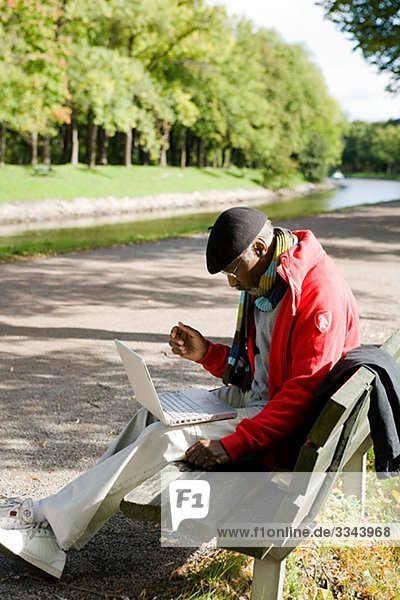Senior man using a laptop on a bench in a park  Sweden.