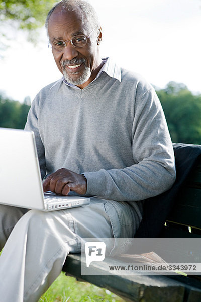 älterer Mann mit einem Laptop in einem Park  Schweden.