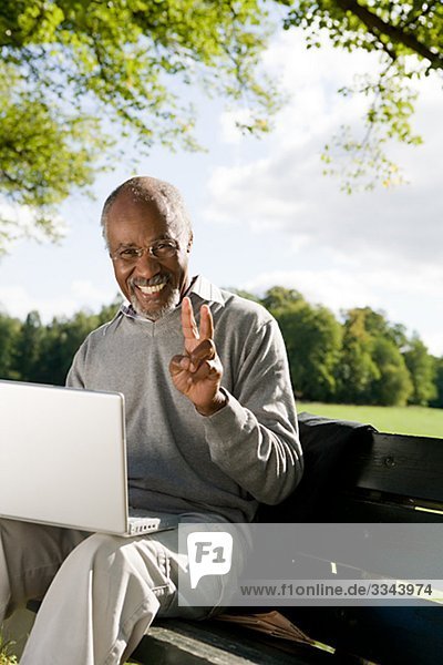 älterer Mann mit einem Laptop in einem Park  Schweden.