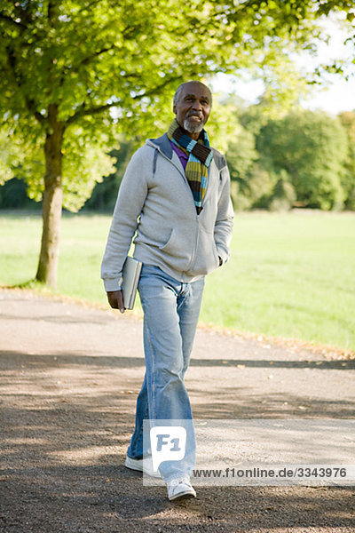 älterer Mann zu Fuß in einem Park mit einem Laptop  Schweden.