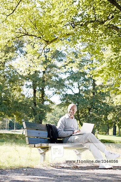 älterer Mann mit einem Laptop in einem Park  Schweden.