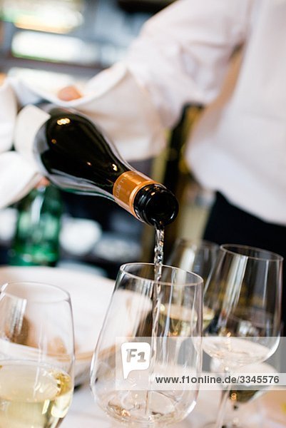 A waiter pouring wine in a glass.