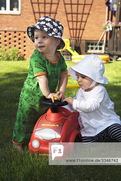 Boy and girl playing with toy car in a garden  Sweden.