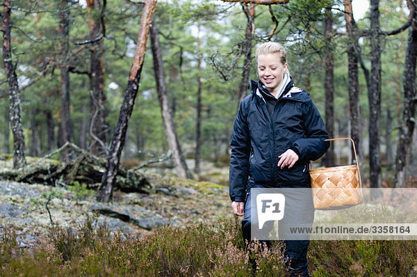 Frau die mit einem Korb im Wald spazieren geht.