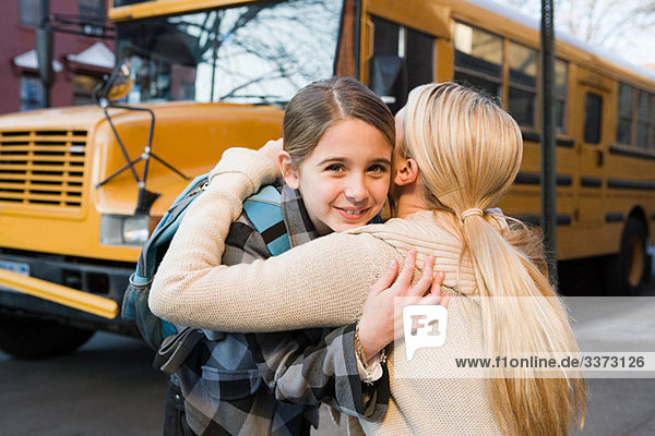 Girl and mother hugging by school bus