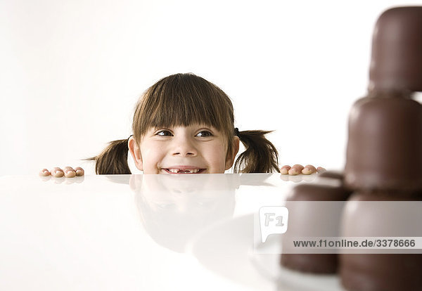 Mädchen schaut über eine Tischkante auf einen Teller mit Schokoküssen