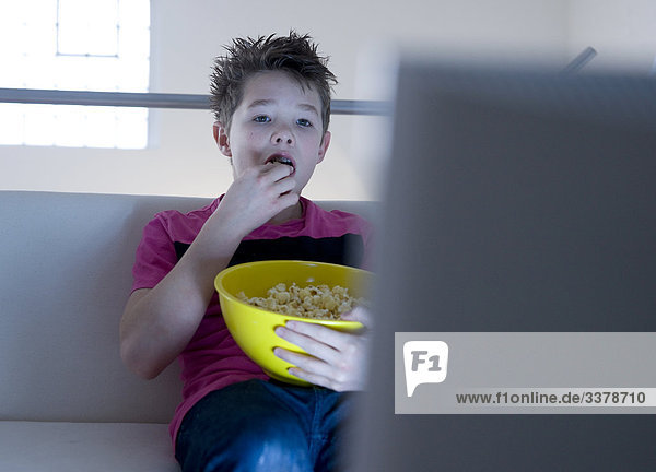 Junge isst Popcorn und schaut Fernsehen