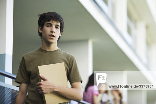 Male high school student carrying binder under arm