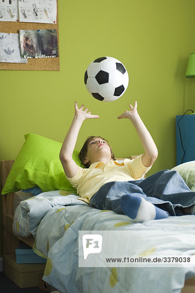 Junge liegt auf dem Bett und wirft den Ball in die Luft.
