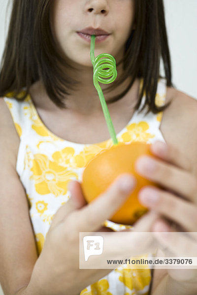 Girl drinking juice from orange half through straw