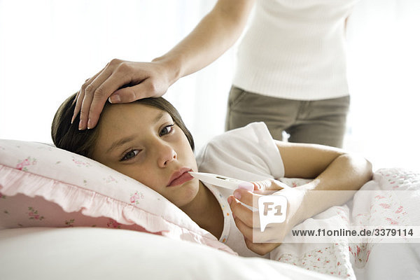 Girl checking temperature with thermometer  mother caressing forehead