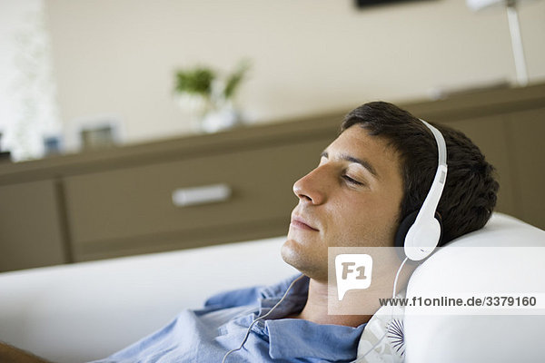 Junger Mann entspannt auf dem Sofa Musik hören mit Kopfhörern